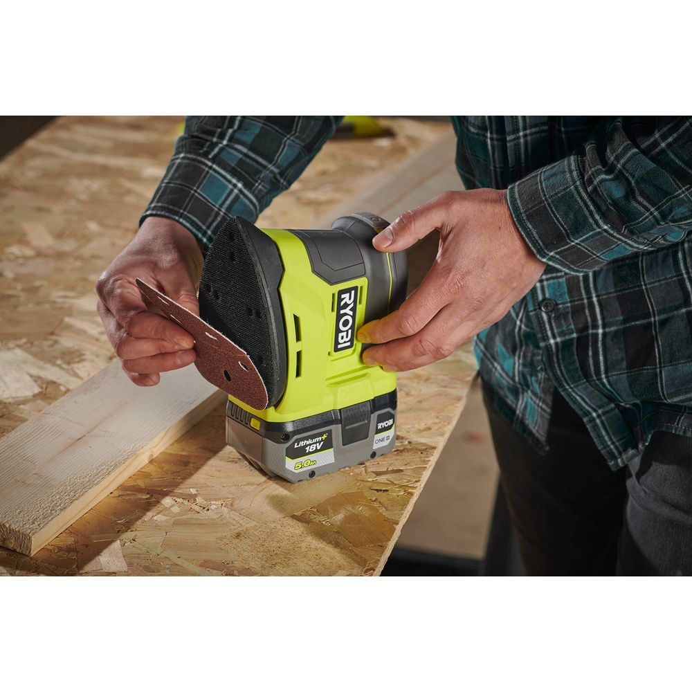 Grüne Ryobi Schleifmaschine mit angebrachter Sandpapier-Scheibe auf einem Holztisch.