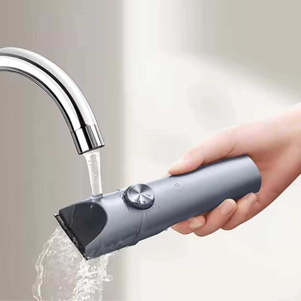 Eine Hand hält einen grauen Haartrimmer unter fließendem Wasser aus einem Wasserhahn.