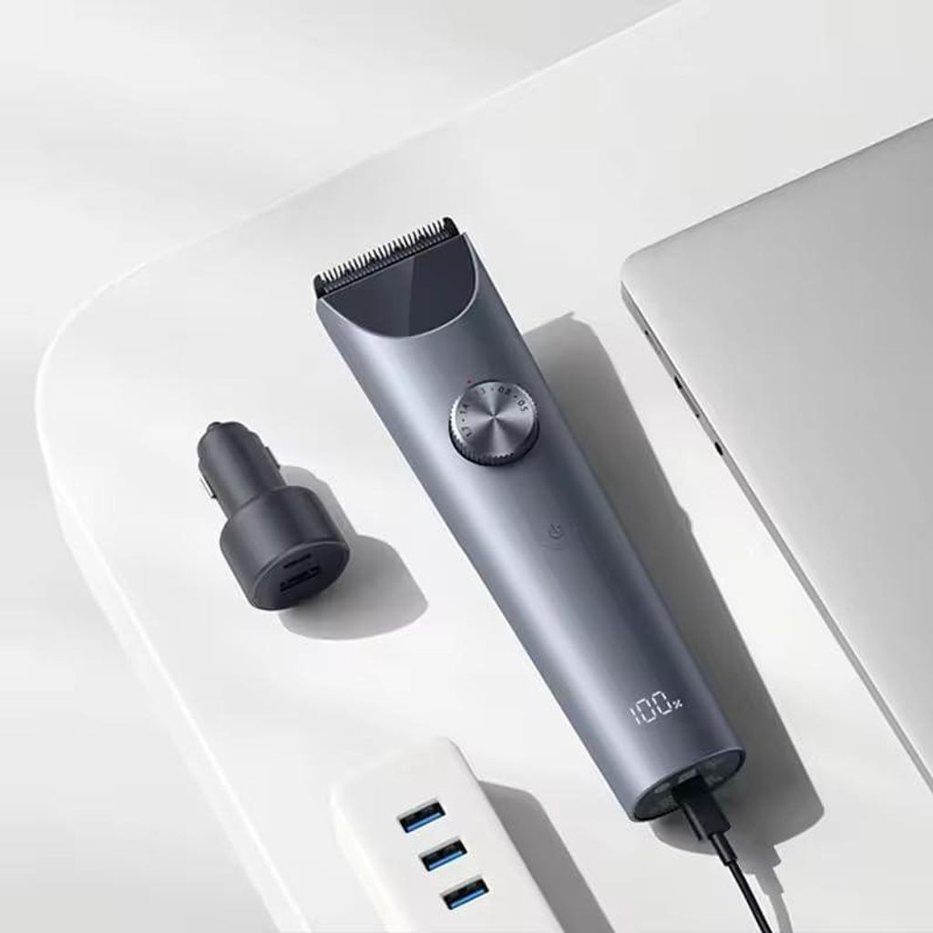 Ein grauer Haarschneider mit 100% Ladung, neben einem Auto-Ladegerät und USB-Hub.