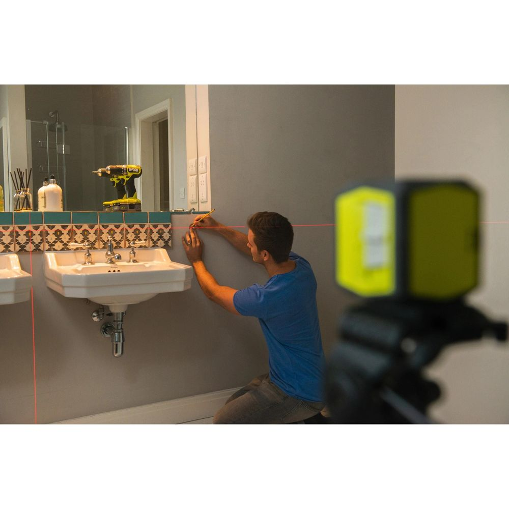 Ein Mann kniet und markiert mit einem Bleistift eine Wand, während ein Laser Nivelliergerät rote Linien projiziert.
