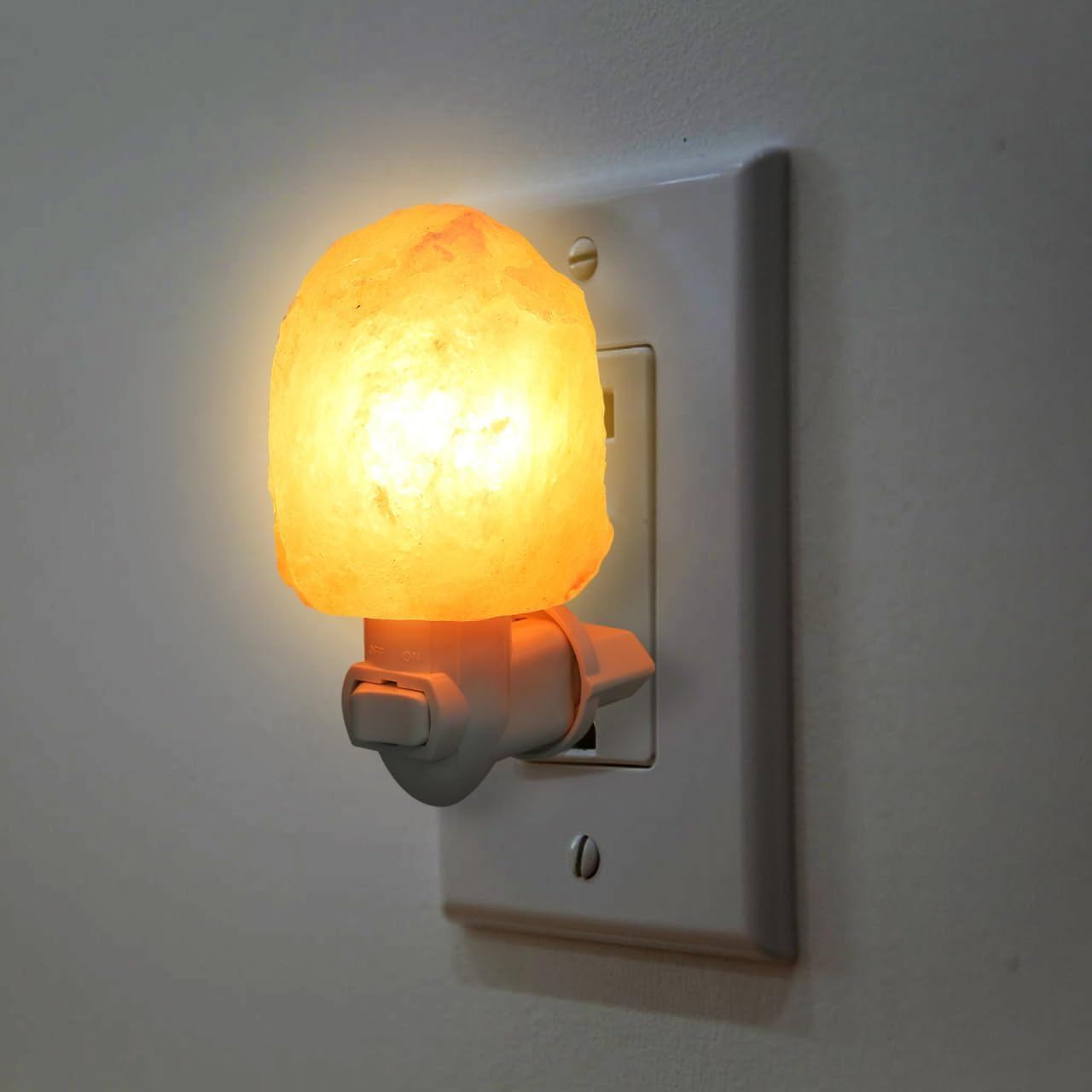 Ein orangefarbener Salzlampen-Nachtlichtstecker leuchtet an einer weißen Wandsteckdose.