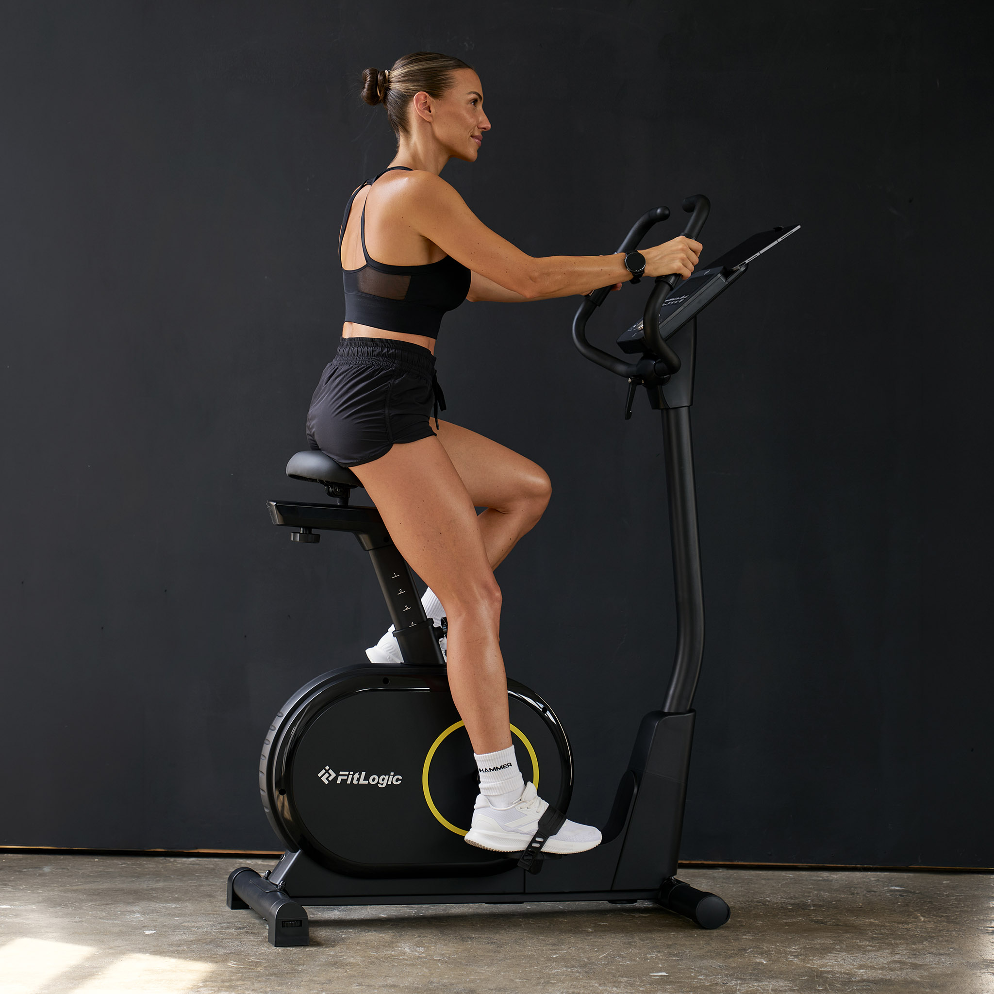 Frau trainiert auf einem schwarzen Heimtrainer vor dunklem Hintergrund.