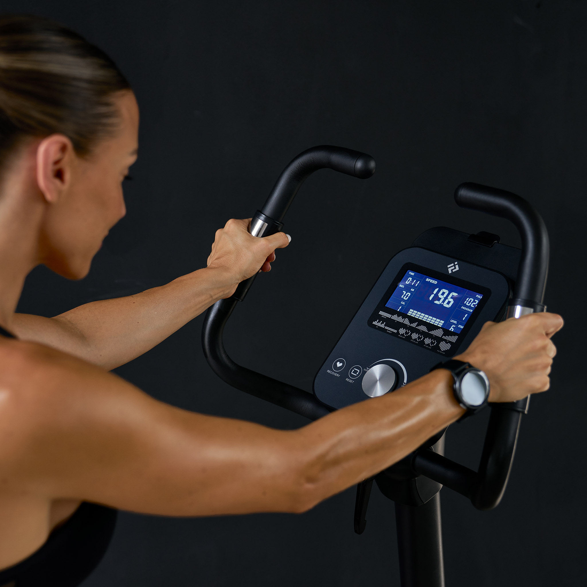 Eine Frau trainiert auf einem Heimtrainer, das Display zeigt Geschwindigkeit und Puls.
