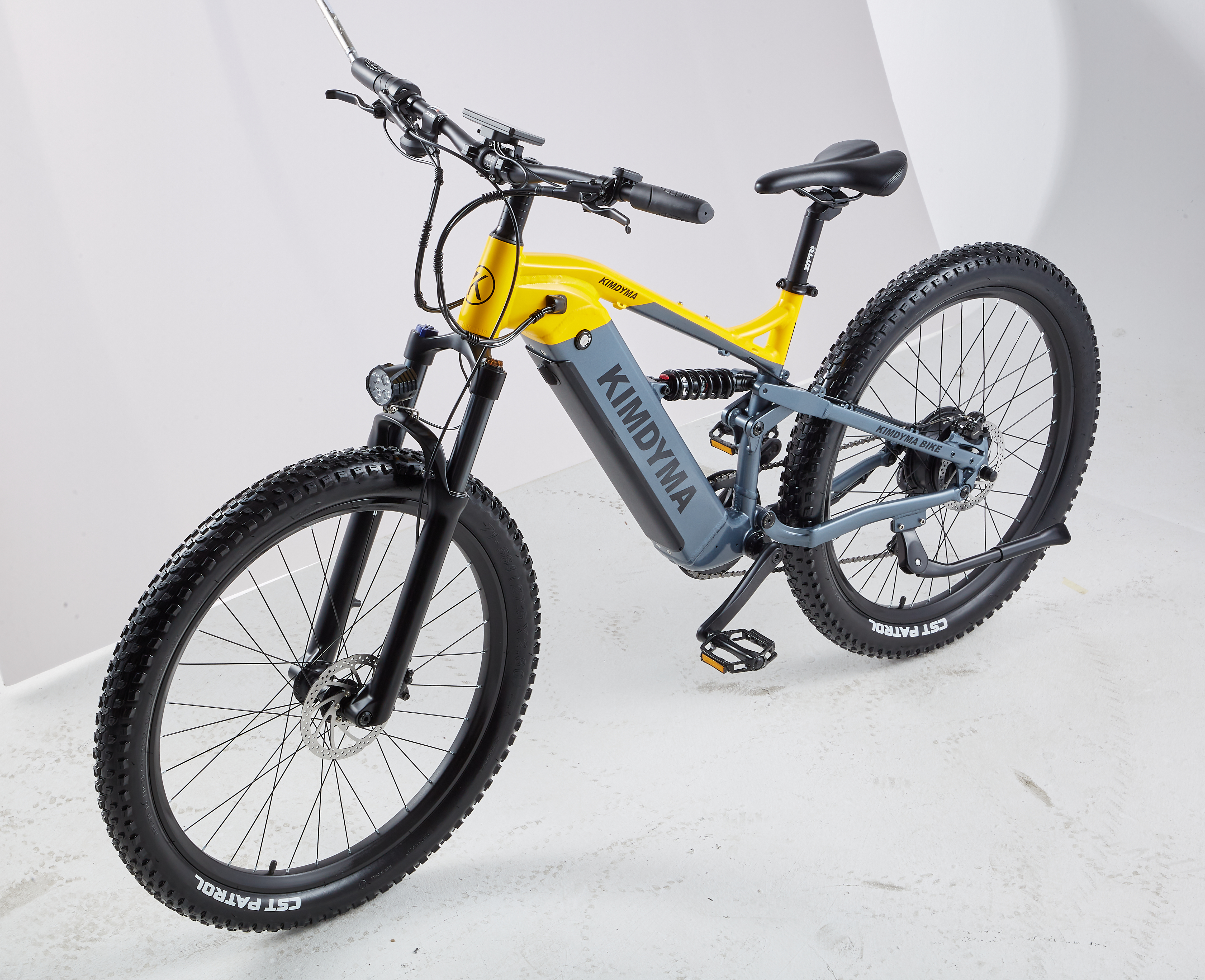 Ein gelbes und graues Mountainbike mit fetten Reifen und Federung steht auf einem weißen Boden.