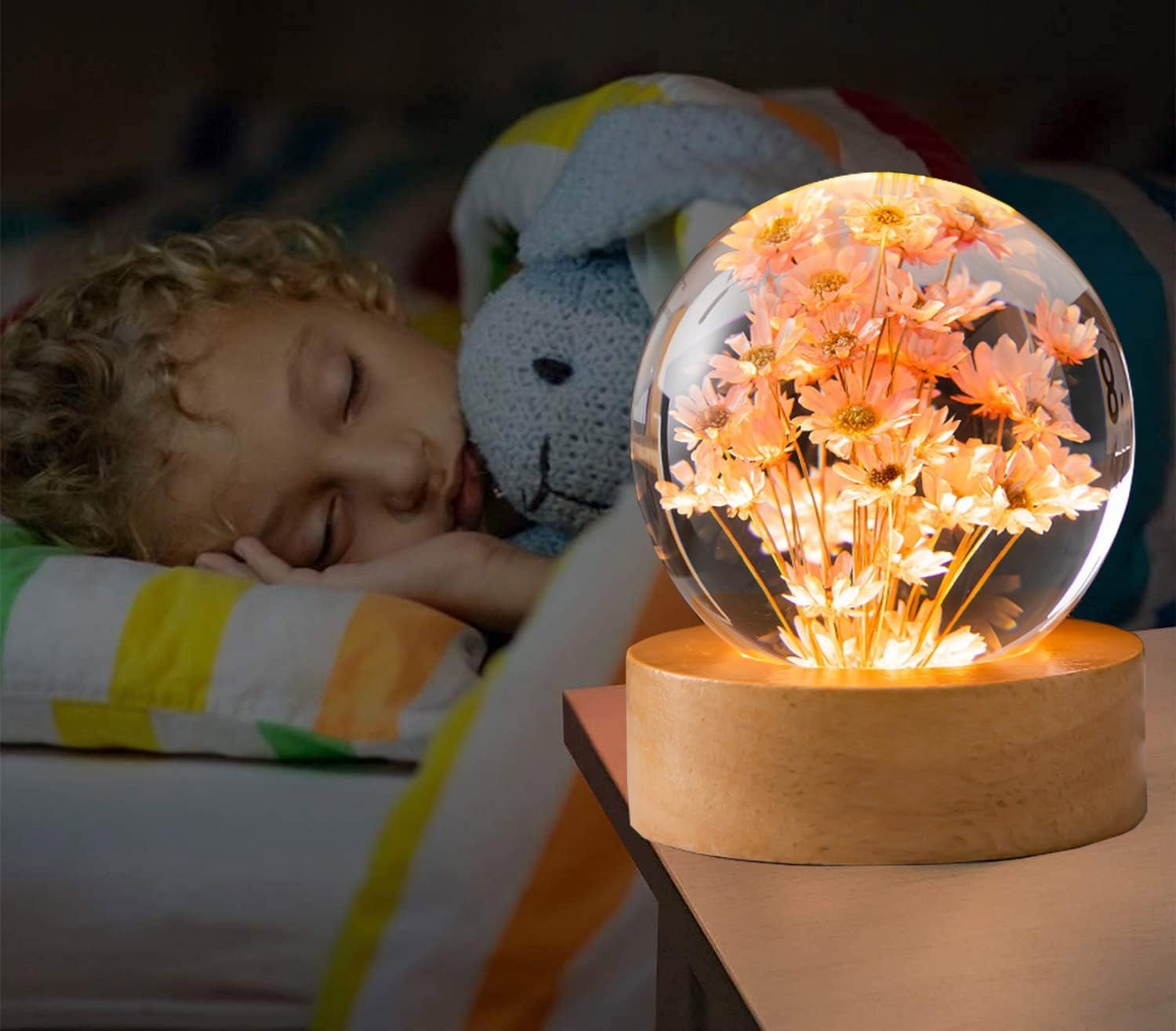 Ein Kind schläft neben einem beleuchteten Glaskugel-Blumendekor auf einem Nachttisch.
