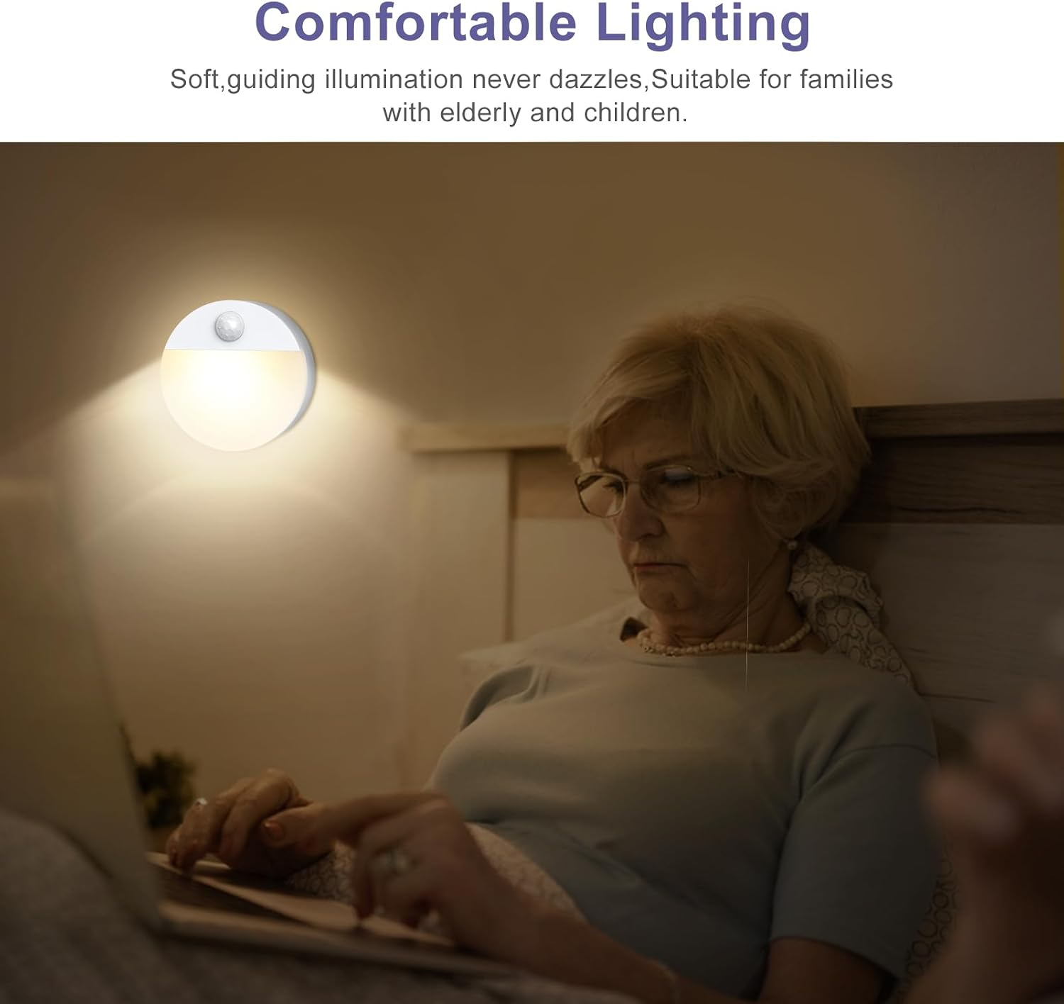 Eine ältere Frau sitzt im Bett und benutzt einen Laptop. Eine Wandleuchte spendet sanftes Licht.