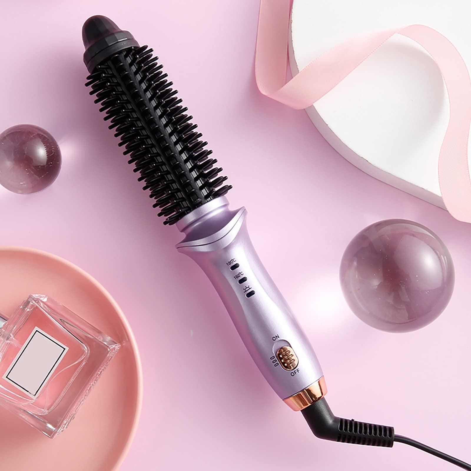 Lila Lockenstab mit schwarzem Bürstenkopf, auf rosa Untergrund mit Parfumflasche und Kugeln.
