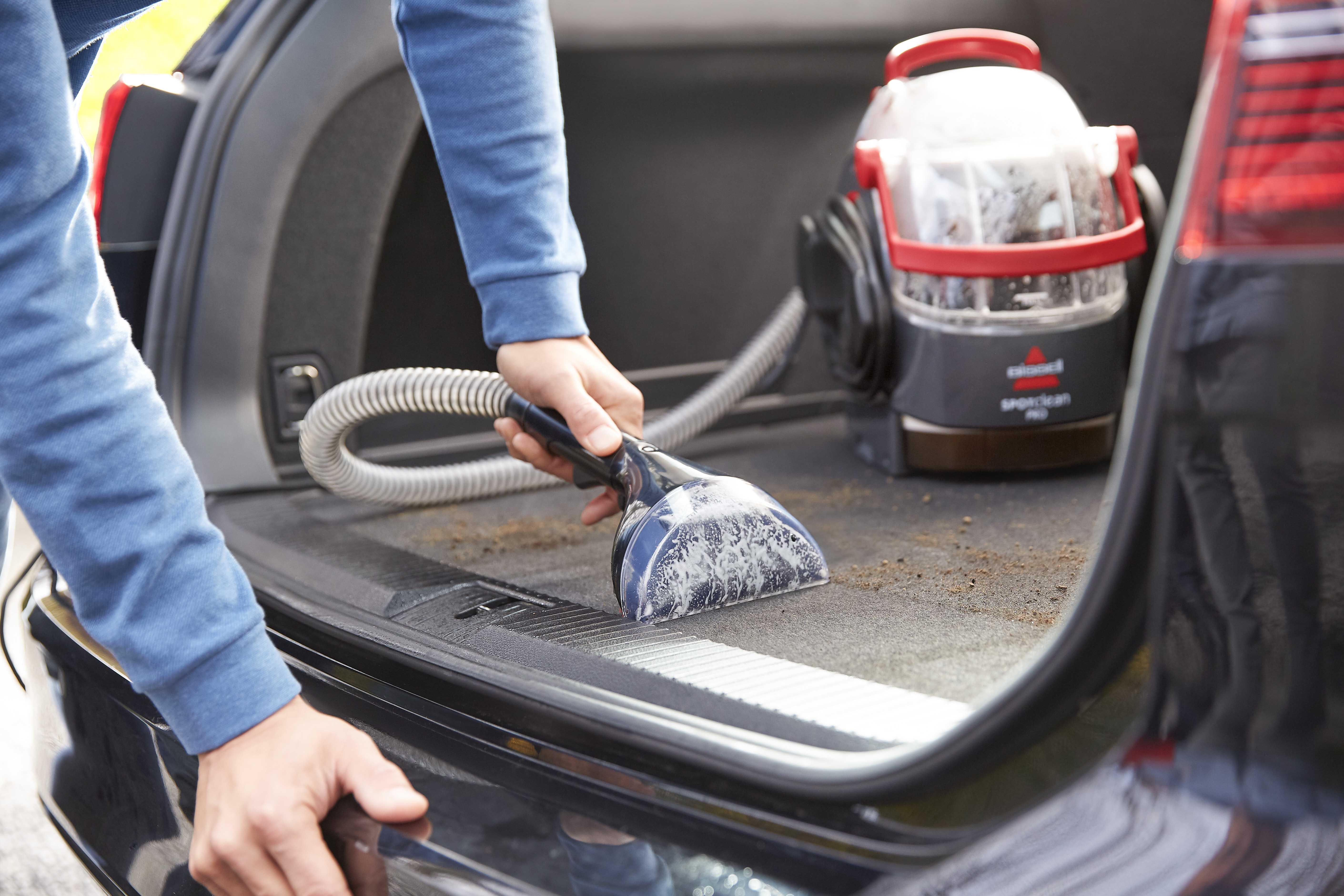 Person reinigt Autokofferraum mit einem Nasssauger. Detailaufnahme.