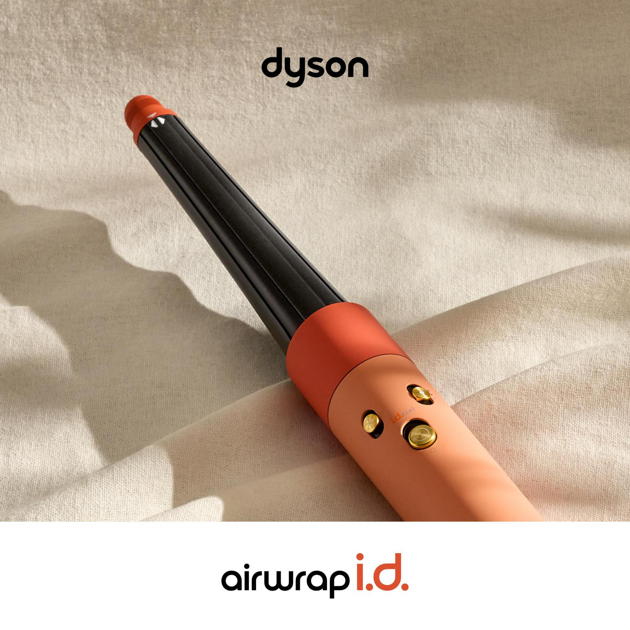 Un arricciacapelli Dyson Airwrap con manico arancione e cilindro nero su tela beige.
