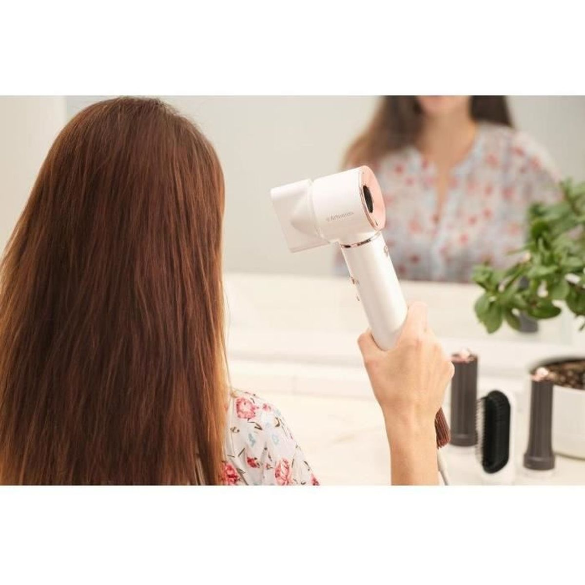 Donna asciuga capelli castani con asciugacapelli bianco davanti allo specchio.