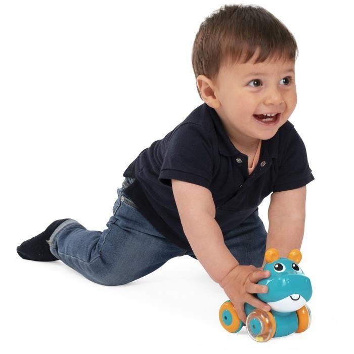 Un niño pequeño con jeans y polo azul marino juega con un hipopótamo de juguete turquesa con ruedas.