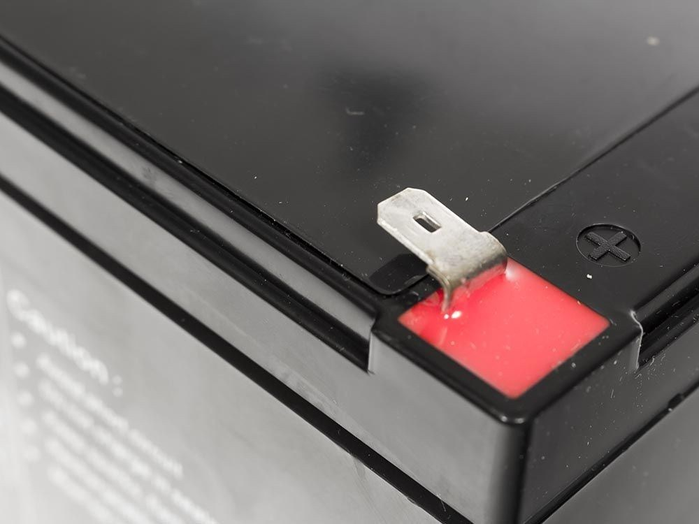 Primer plano de una batería negra con terminal de metal y aislamiento rojo.