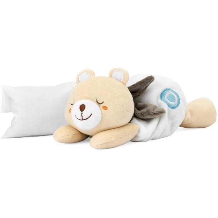 Un orsacchiotto beige giace accanto a un cuscino e una coperta bianchi.