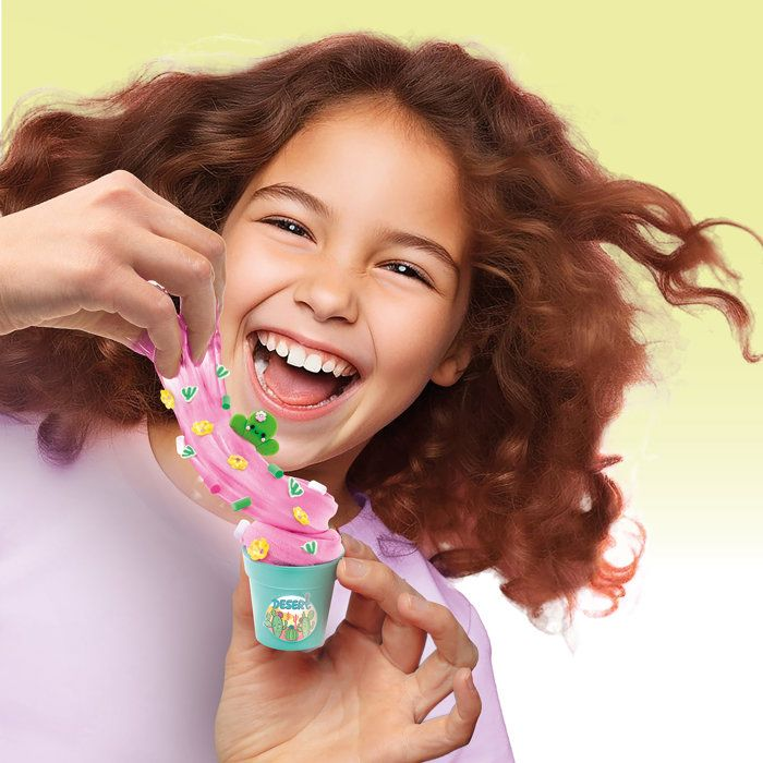 Una niña riendo con pelo castaño largo juega con masa rosa.