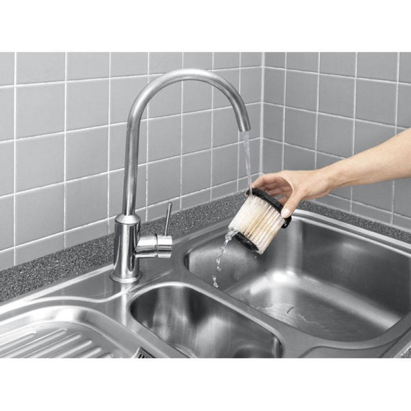 Una mano sciacqua un filtro bianco sporco sotto un rubinetto argentato in un lavello in acciaio inox.
