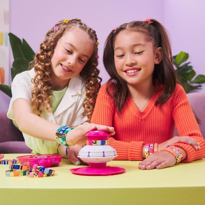 Dos niñas hacen pulseras. Una usa un aparato rosa, la otra mira.
