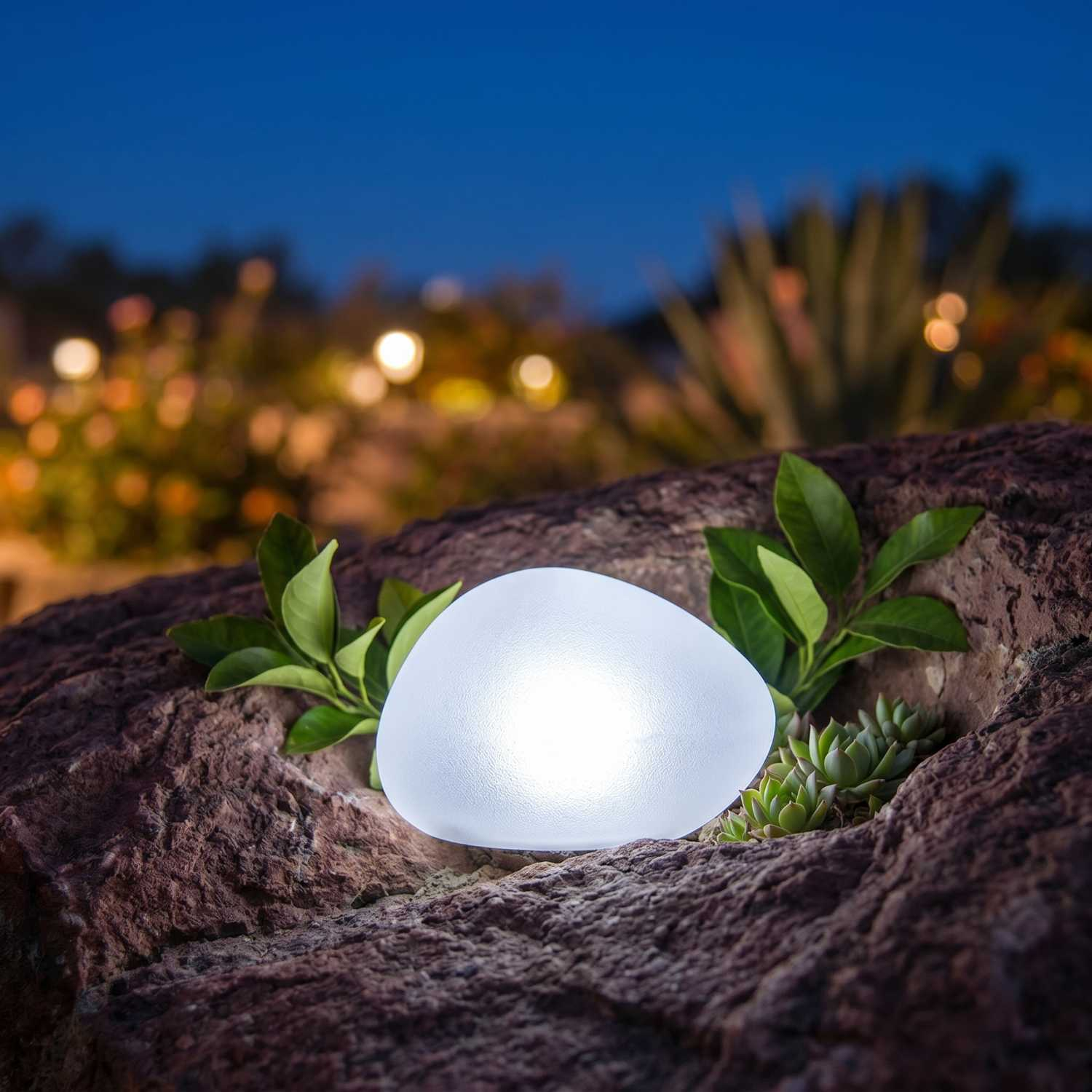 Eine leuchtende, eiförmige Lampe sitzt auf Steinen mit grünen Blättern und Sukkulenten.