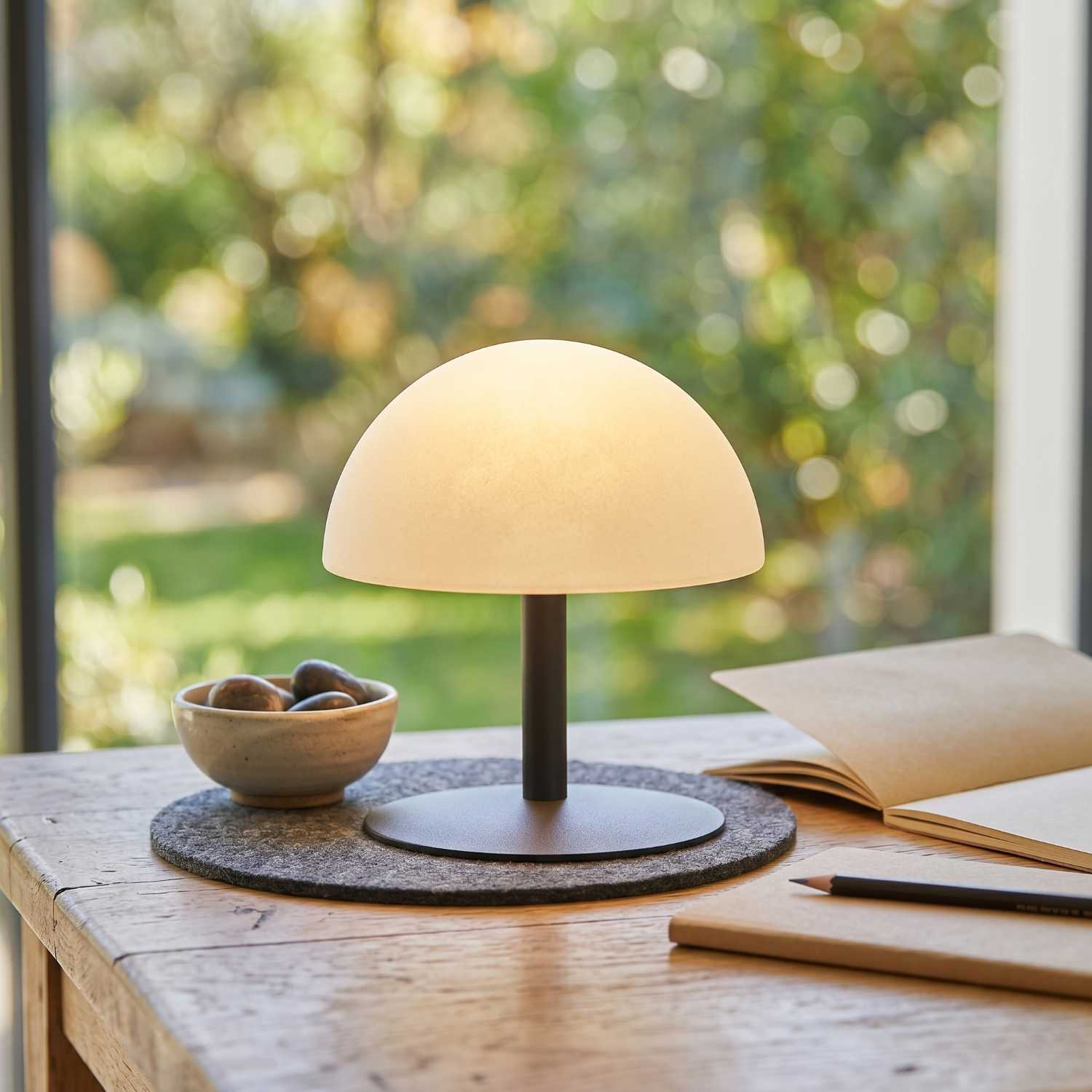 Eine moderne Pilzlampe auf einem Holztisch mit einer Steinschale und einem offenen Notizbuch.