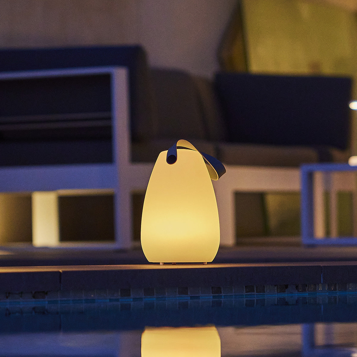 Eine leuchtende Lampe steht am Poolrand mit Spiegelung im Wasser.