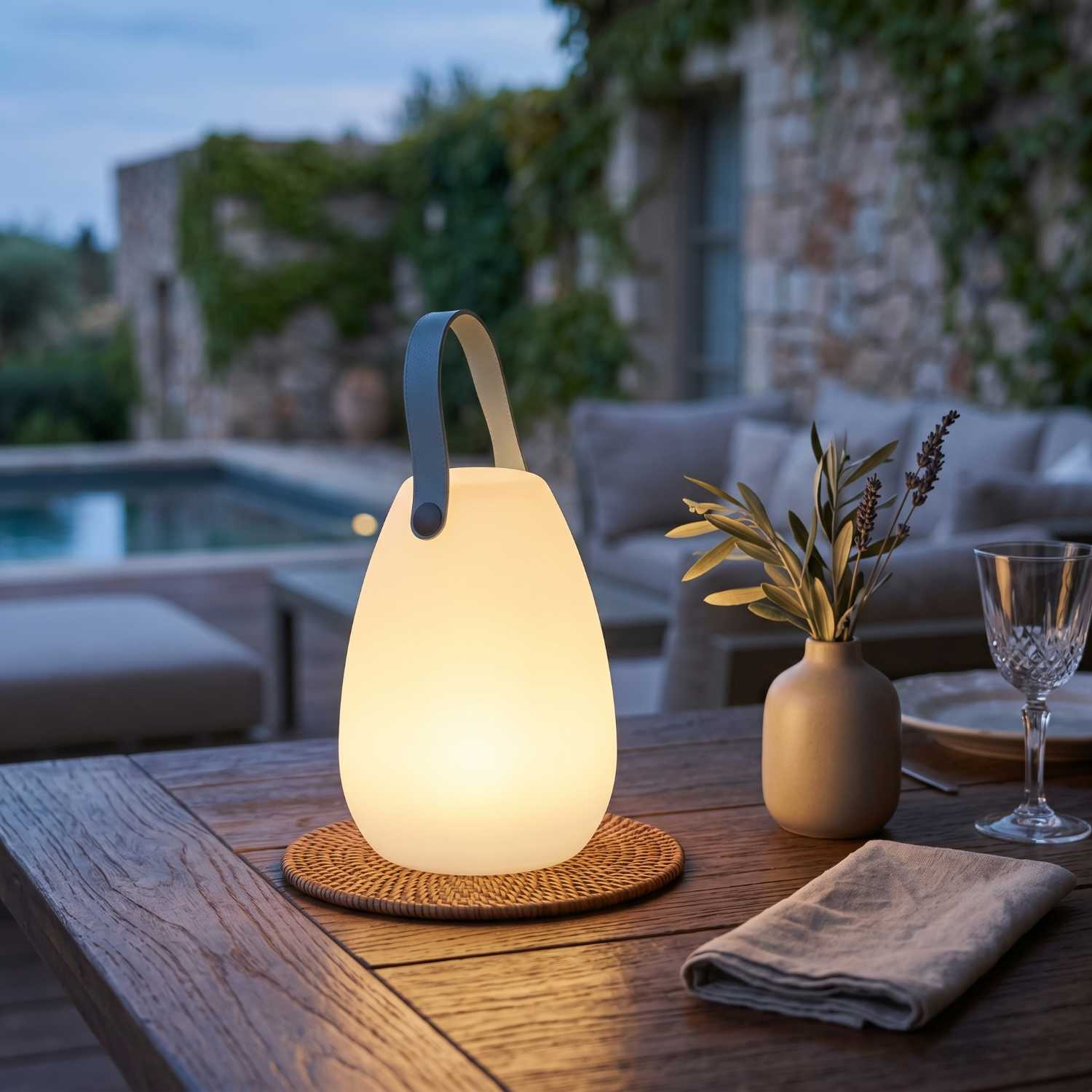 Eine beleuchtete Laterne auf einem Holztisch mit Vase und Glas im Freien.