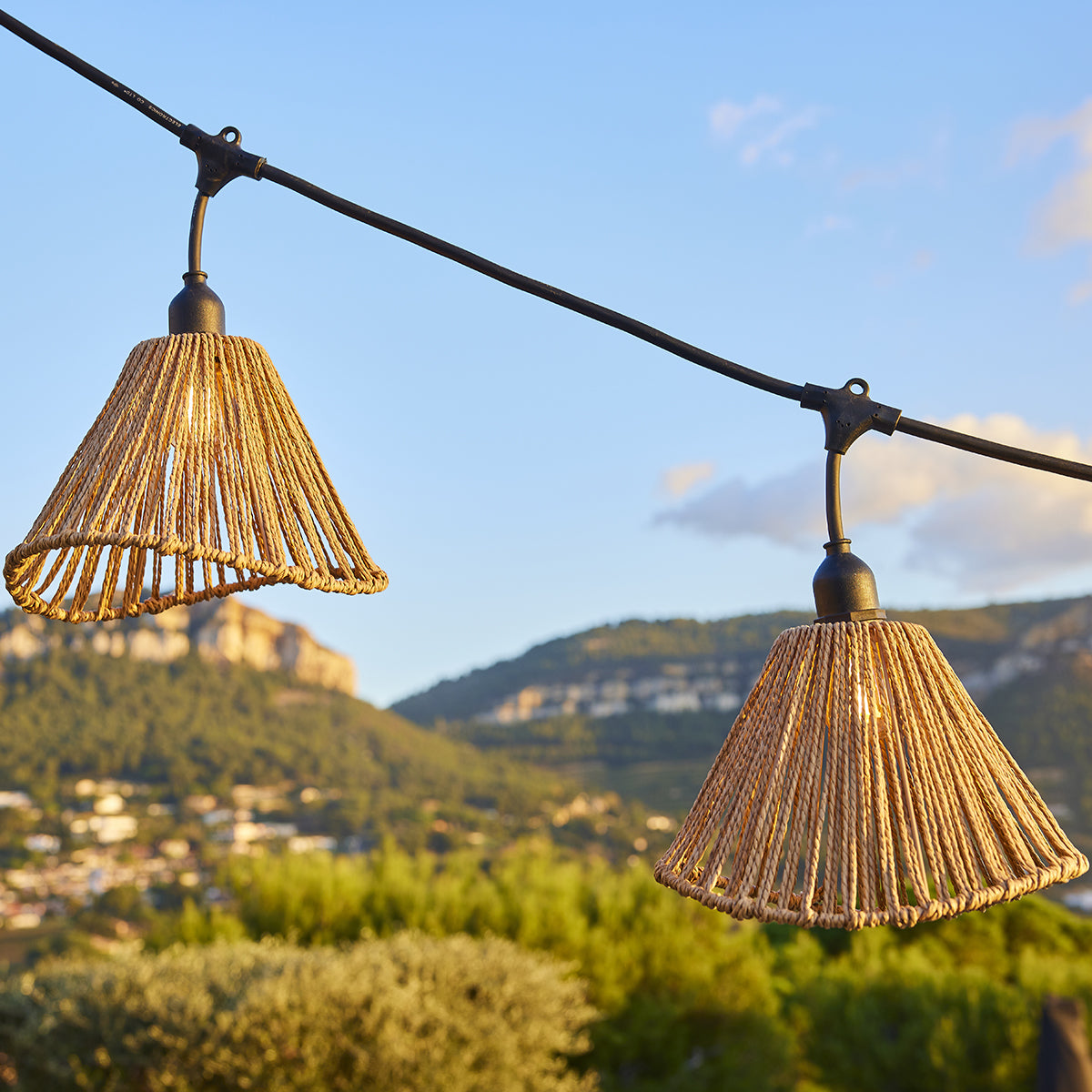Zwei Laternen aus Seil hängen an einem Kabel vor einem Bergpanorama.