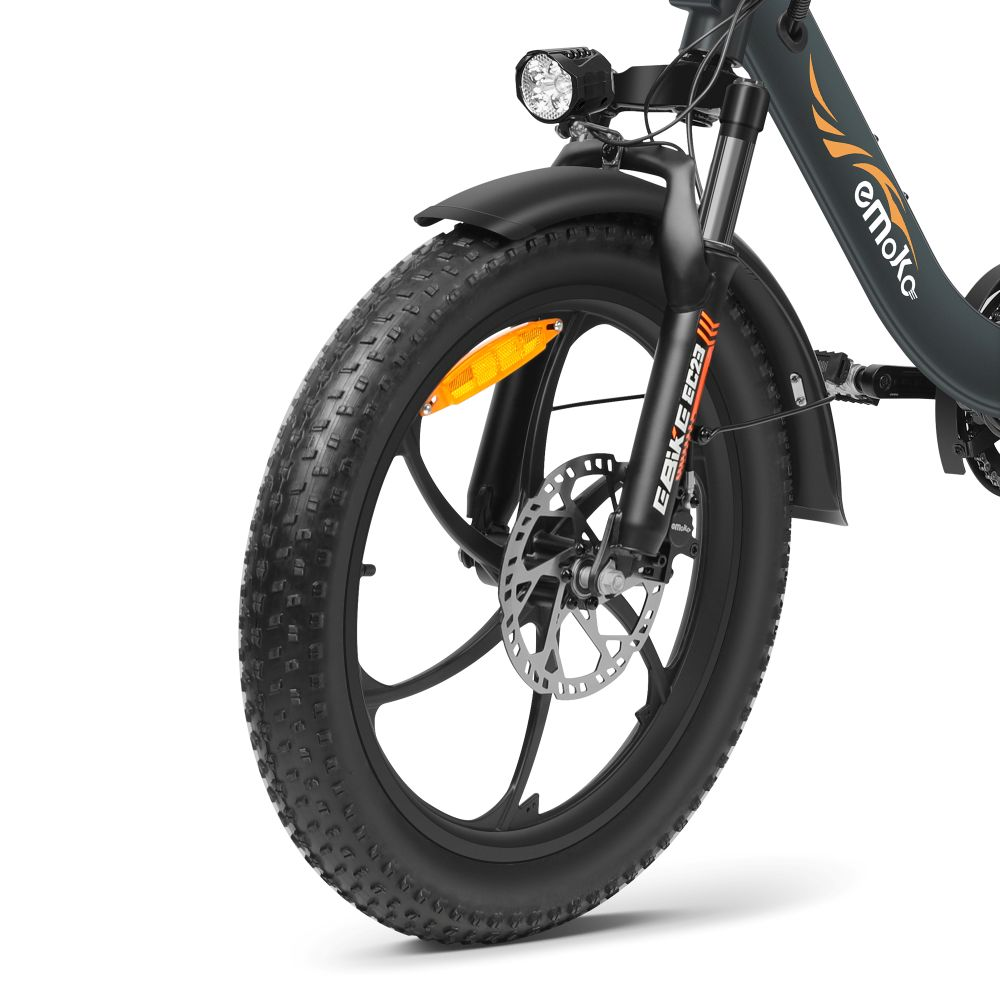 Ruota anteriore e forcella di una e-bike scura con freno a disco e faro.