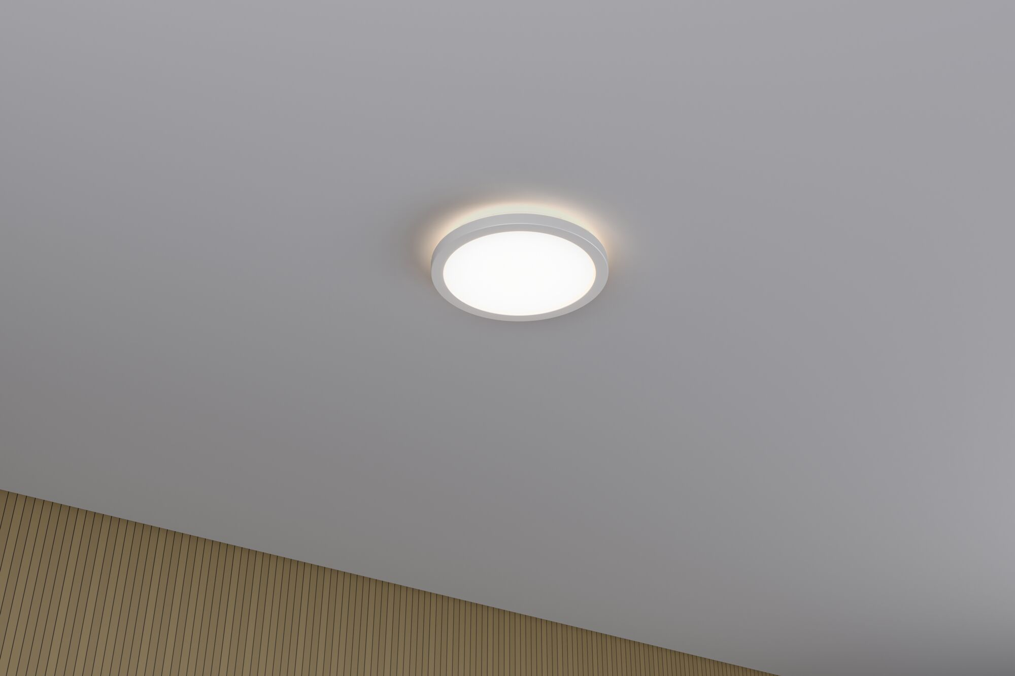 Eine weiße Deckenleuchte leuchtet auf einer Decke über einer Holzwand.