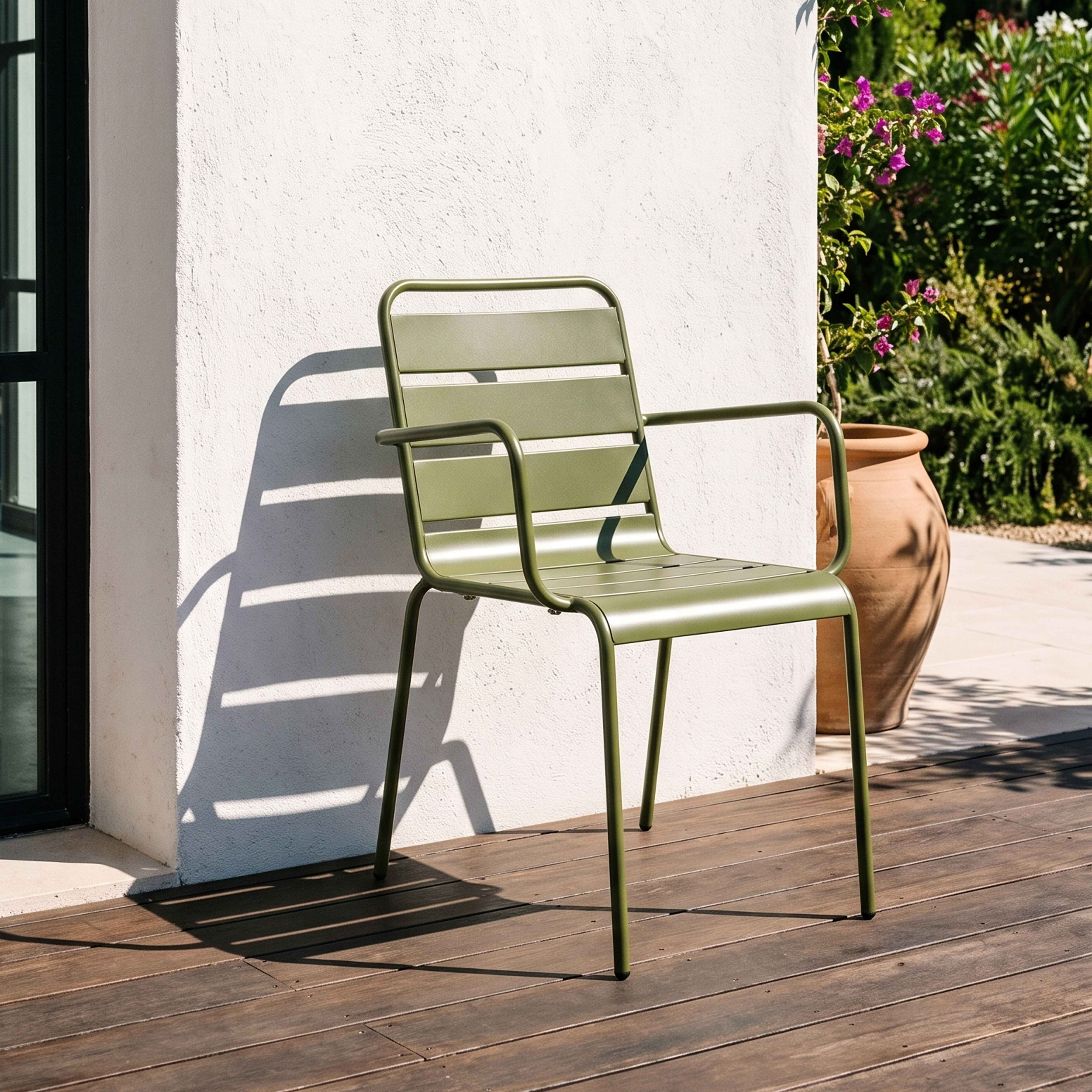 Ein grüner Metallstuhl steht auf einer Holzterrasse neben einer weißen Wand und Pflanzen.