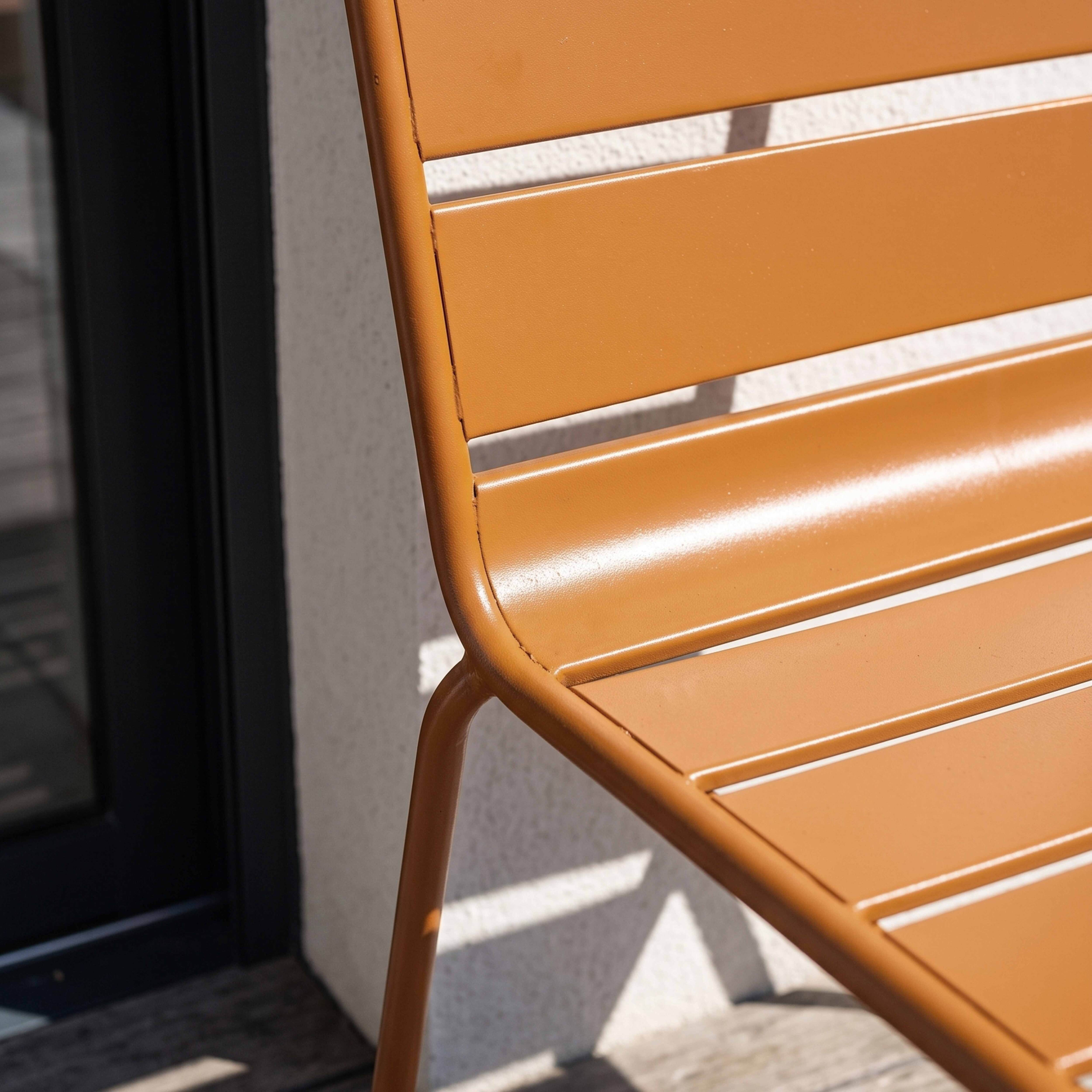 Orange Metallstuhl mit Lamellen auf einem Holzboden, Schatten fällt auf Wand.