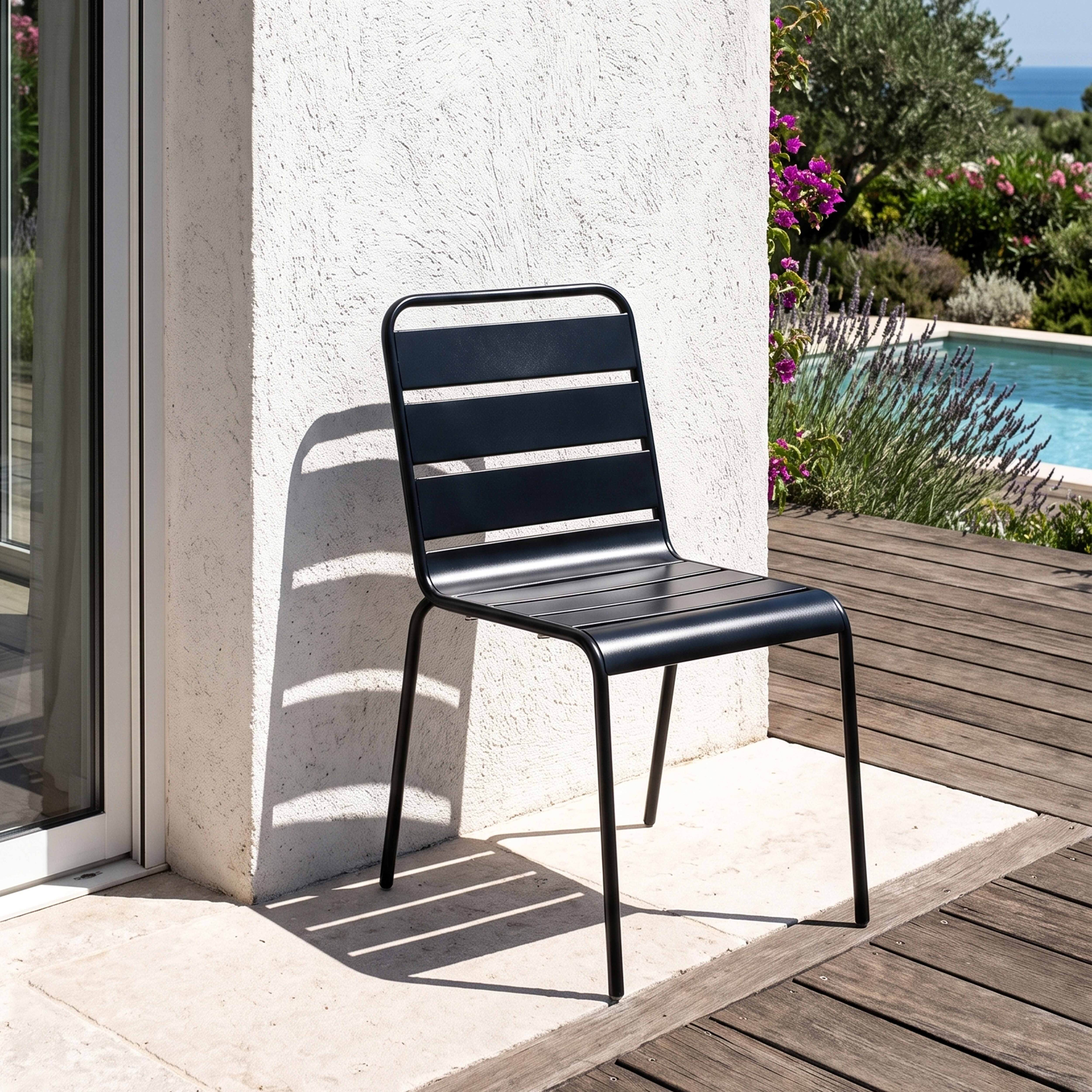 Ein schwarzer Metallstuhl steht auf einer Steinterrasse neben einem Pool und Garten.