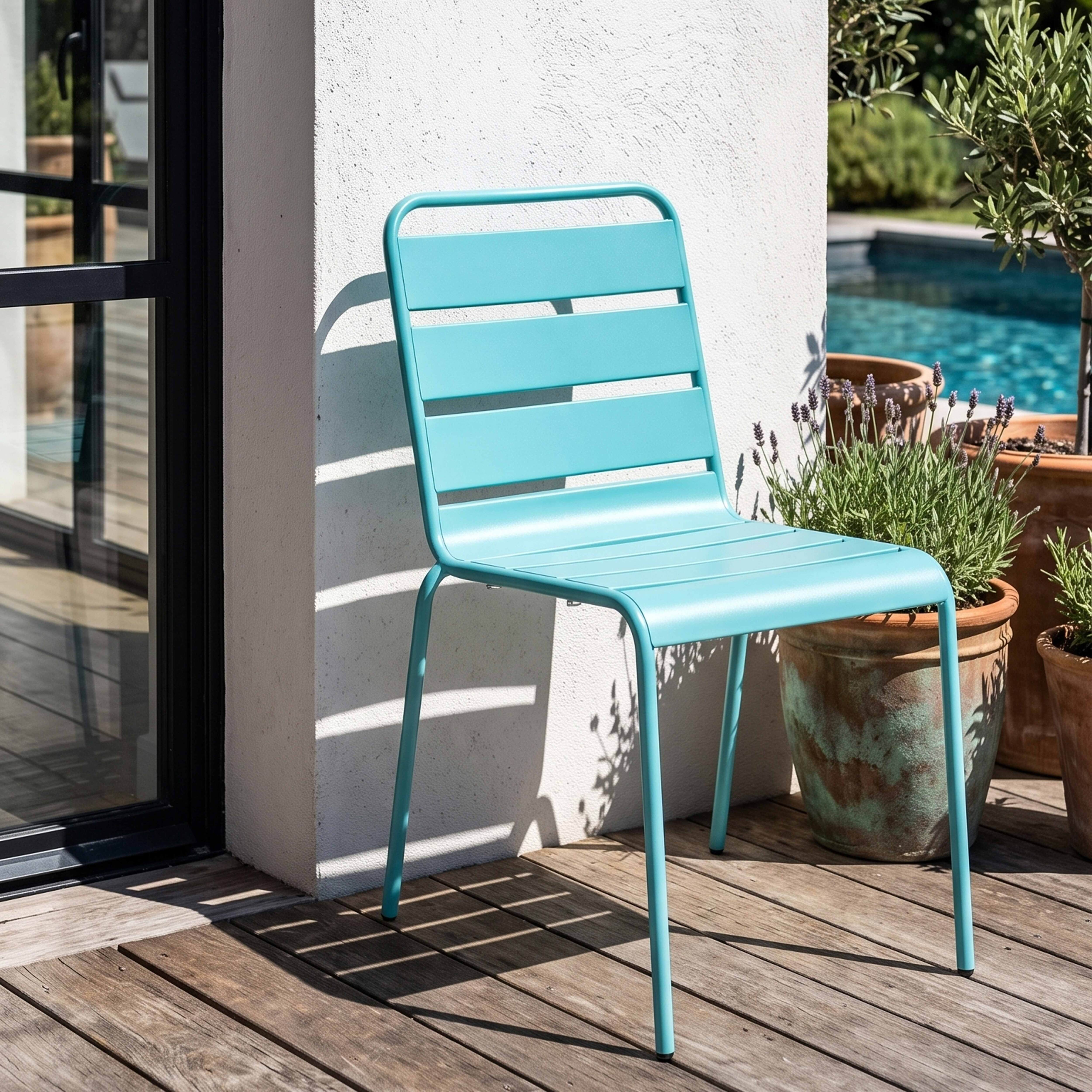 Ein türkisfarbener Stuhl steht auf einer Holzterrasse neben Pflanzen und einem Pool.