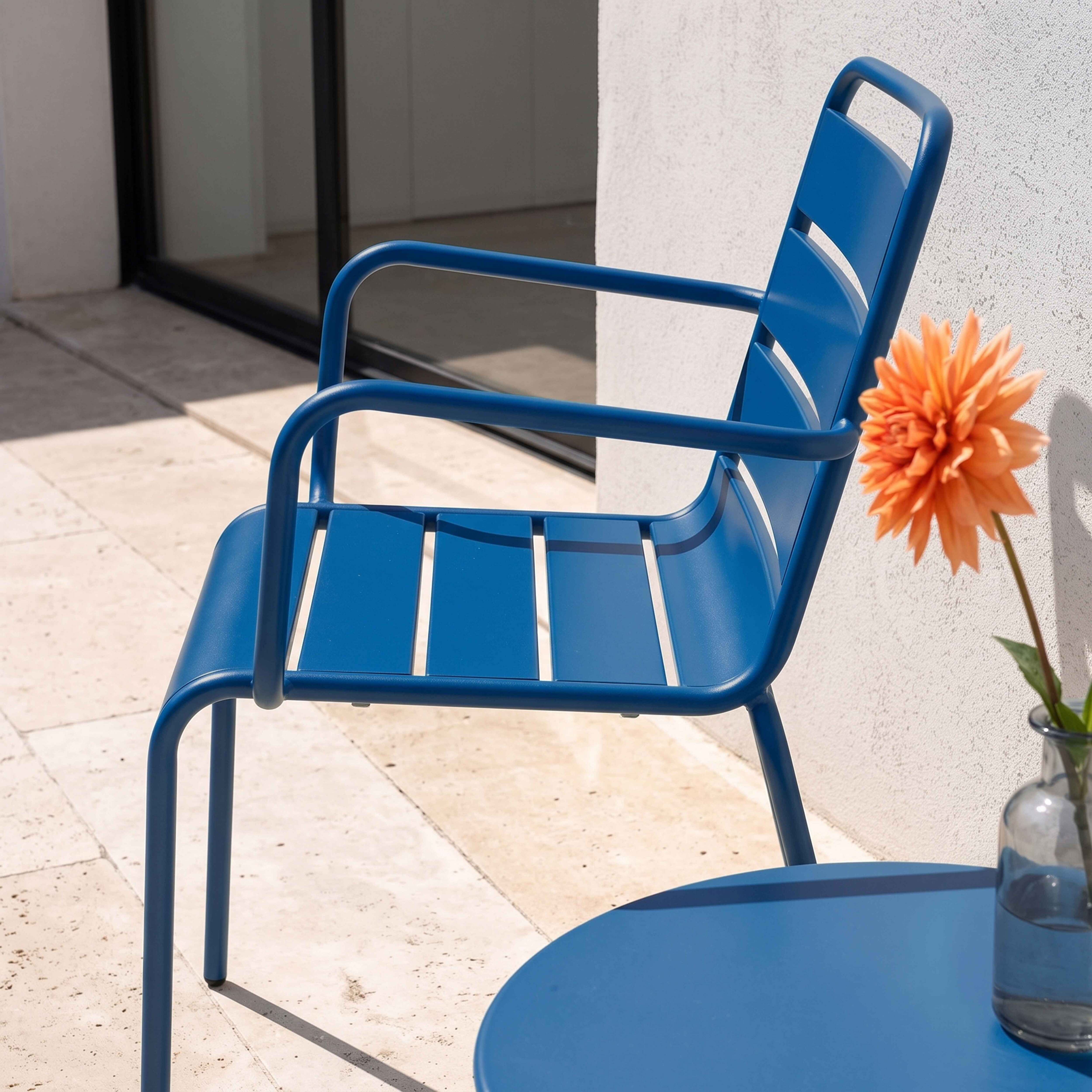 Ein blauer Metallstuhl und ein Tisch im Freien mit einer orangefarbenen Blume.