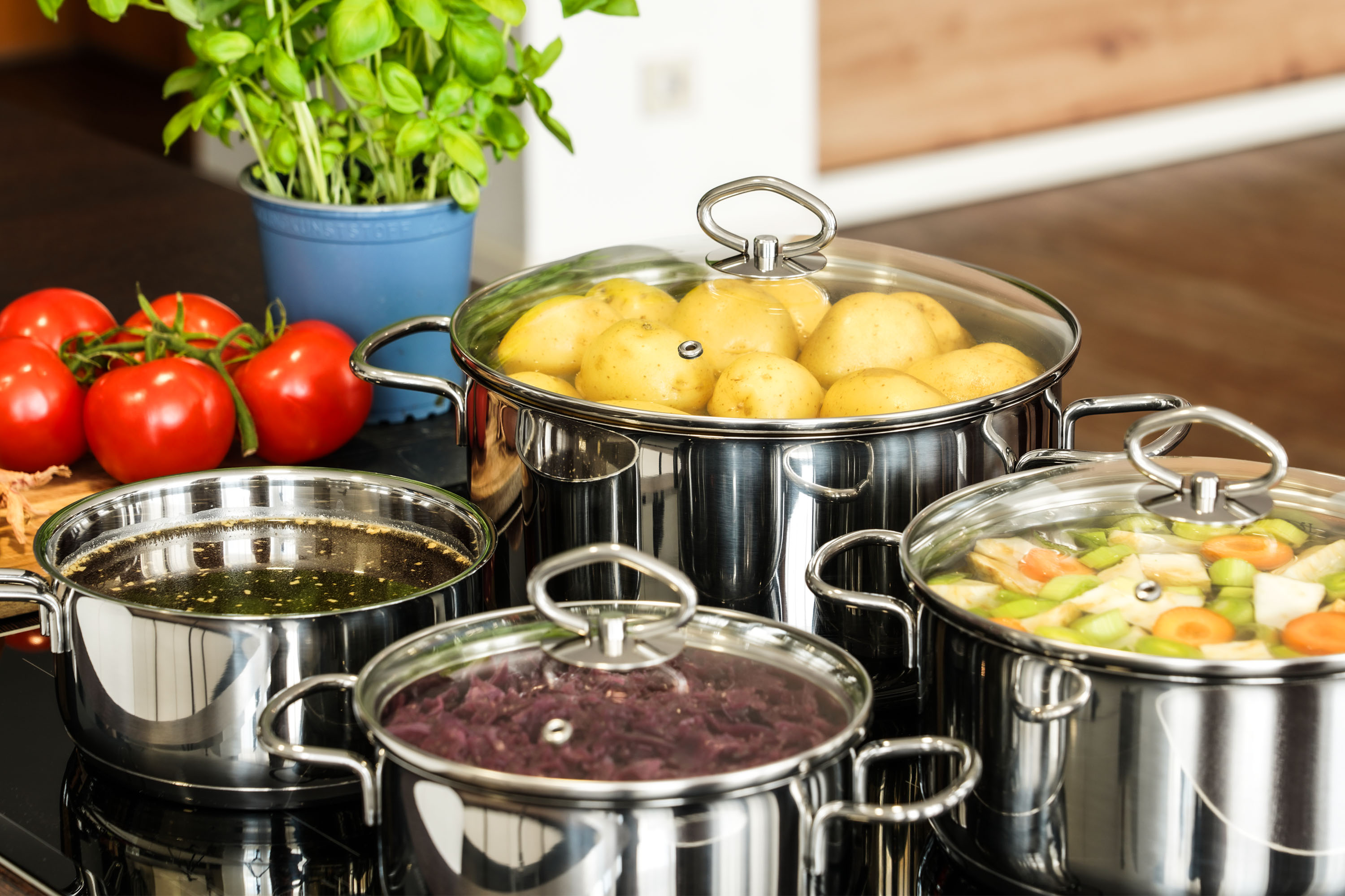 Mehrere Kochtöpfe auf einem Herd, gefüllt mit Kartoffeln, Gemüse, Rotkohl und Brühe.