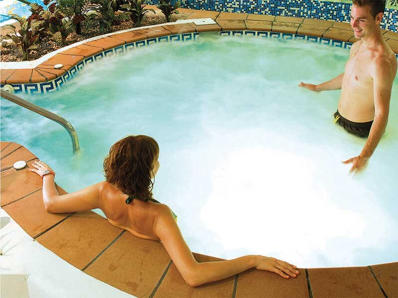 Un hombre y una mujer se relajan en un jacuzzi humeante con paredes de azulejos azules.