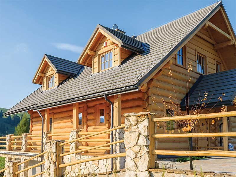 Una gran casa de troncos de madera con pilares de piedra y valla de madera.
