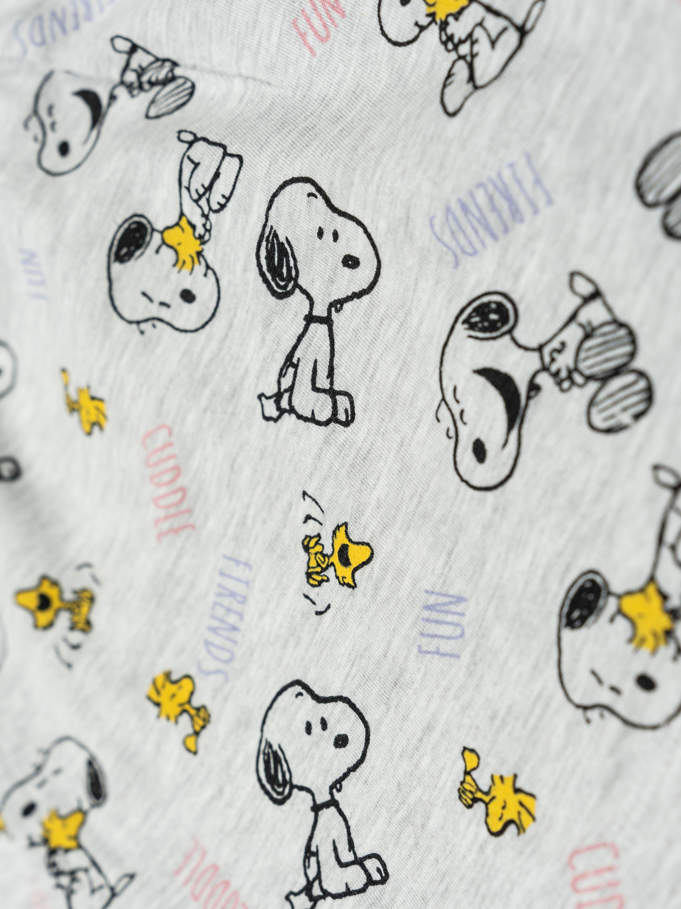 Ein hellgrauer Stoff mit einem Muster aus Snoopy-Hunden und Woodstock-Vögeln.