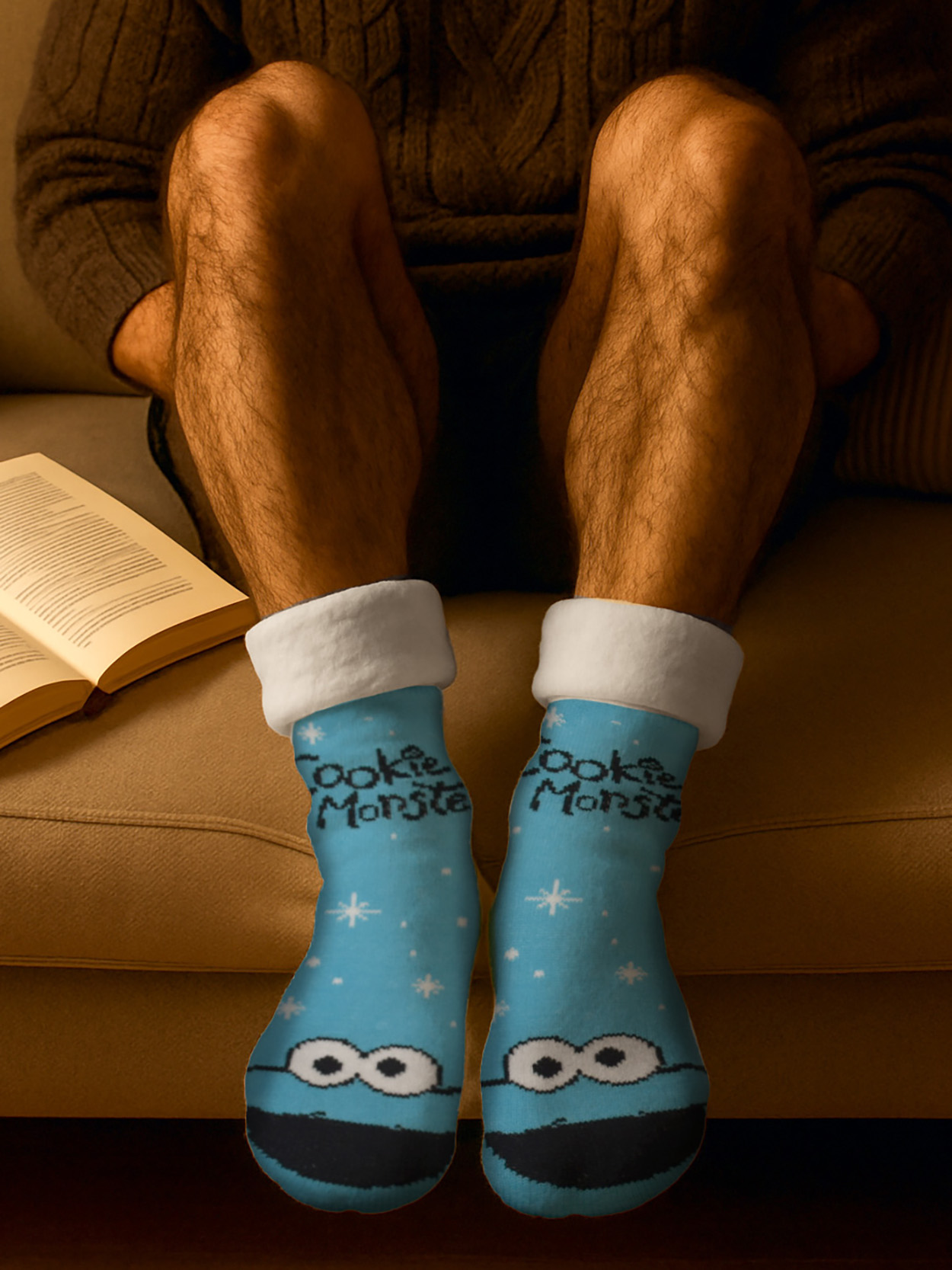 Mann in blauen Socken mit Cookie Monster Motiv sitzt auf Sofa mit Buch.