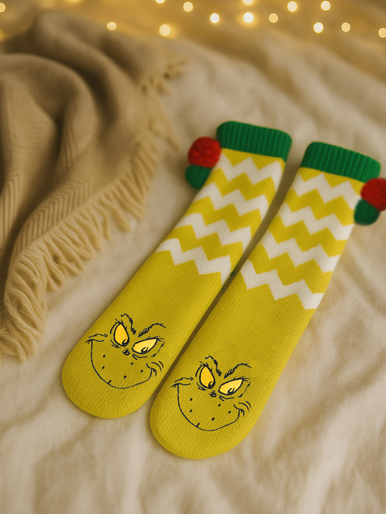 Gelbe Socken mit Grinch-Motiv, Zickzackmuster und roten Bommeln.