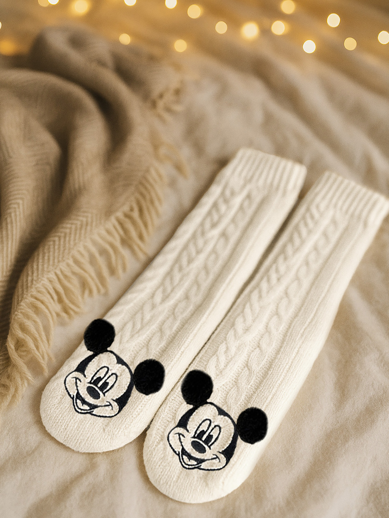 Cremefarbene Socken mit Mickey-Maus-Motiv auf einer Decke mit Lichtern.