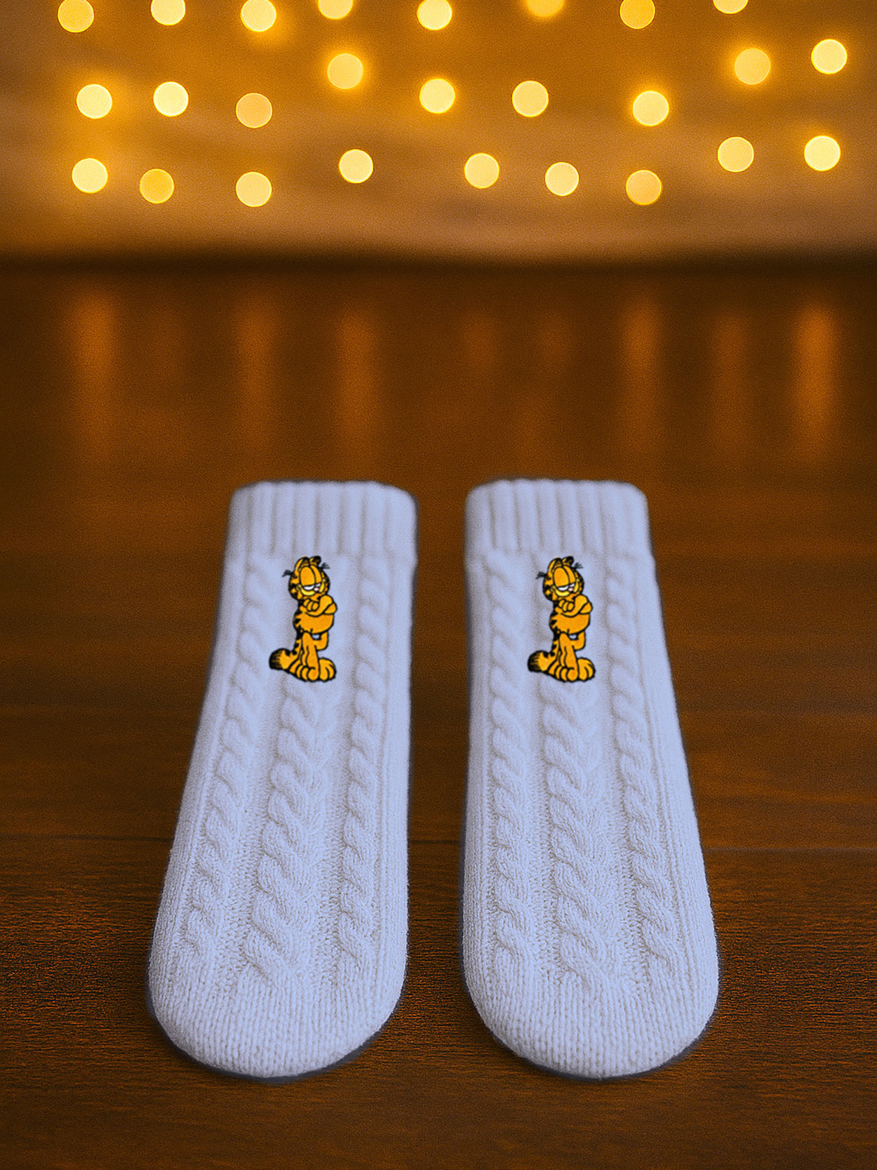 Zwei weiße Stricksocken mit Garfield-Motiv auf Holzhintergrund.