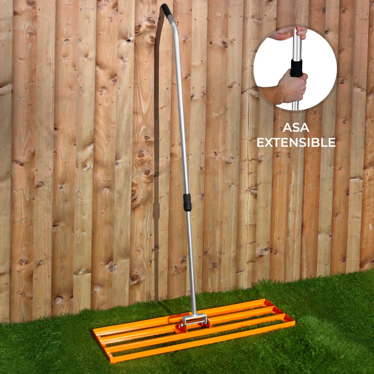 Rastrillo naranja para césped con mango metálico extensible sobre césped frente a valla de madera.