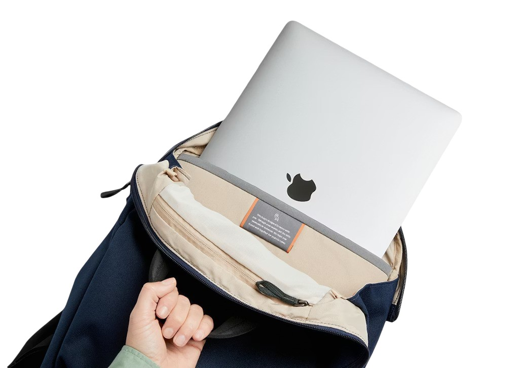 Srebrny laptop z logo Apple wkładany do granatowego plecaka.