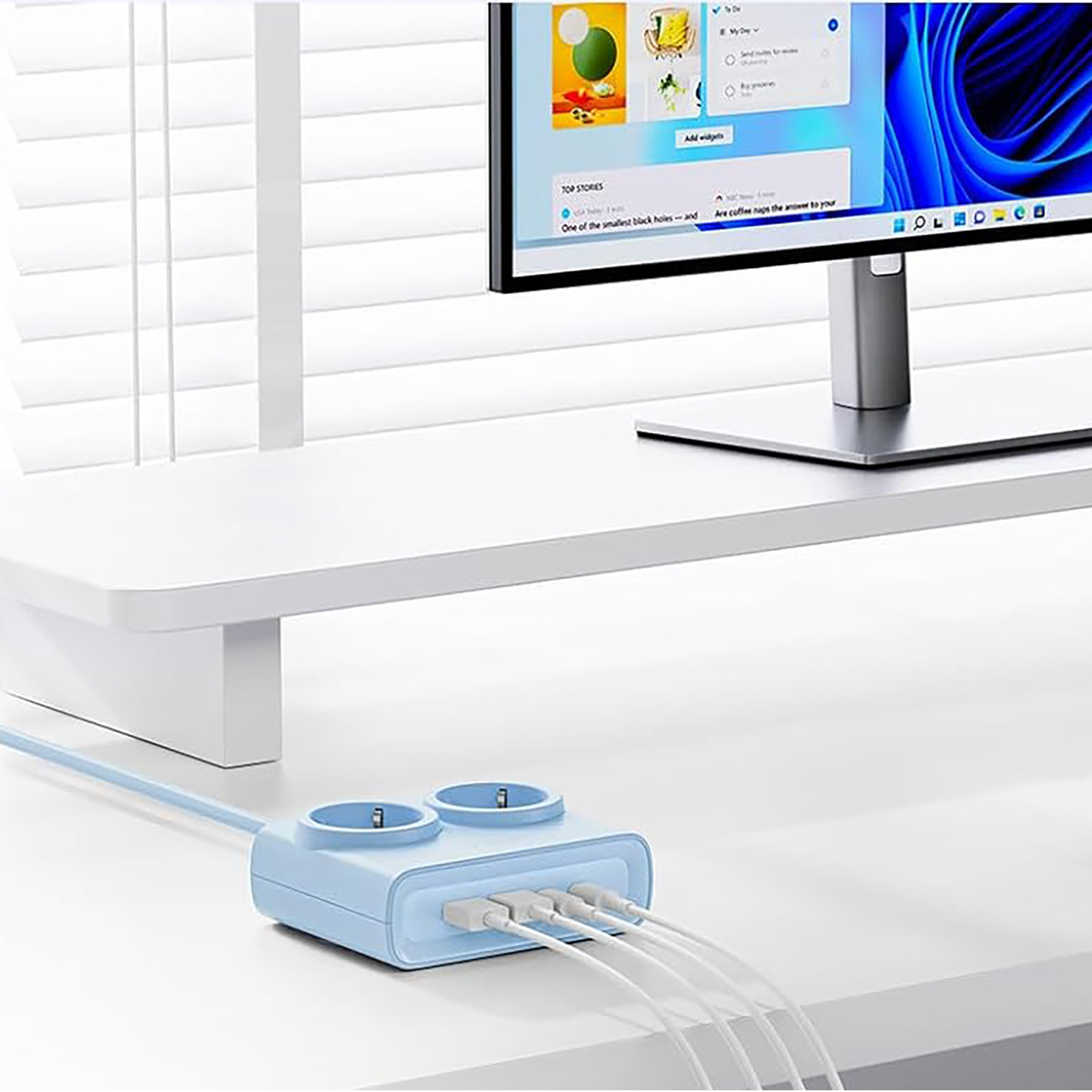 Niebieska listwa zasilająca z portami USB znajduje się na biurku obok monitora.