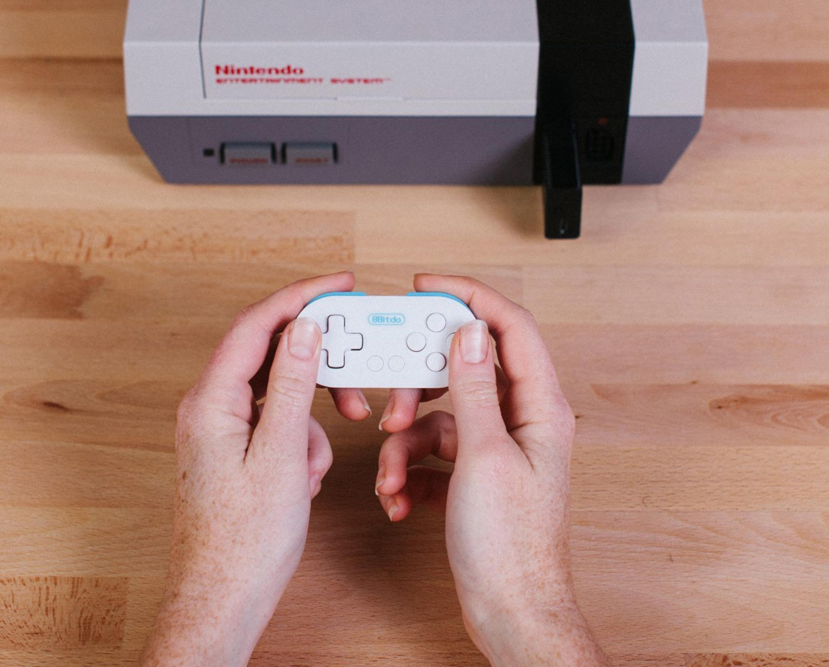 Osoba trzyma biały kontroler przed szarym systemem Nintendo Entertainment.