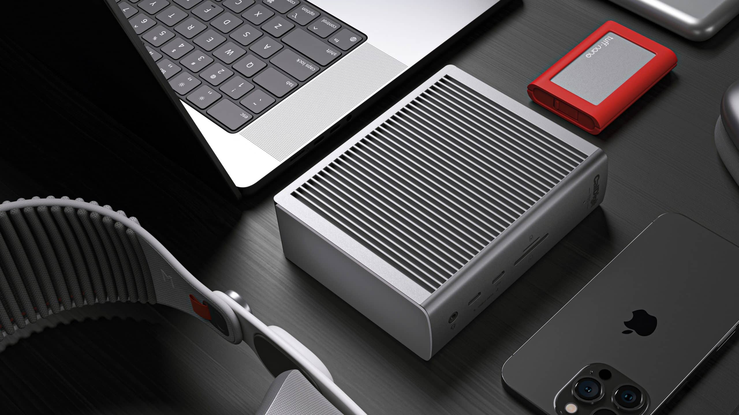 Srebrna klawiatura laptopa, szary mini PC, czerwony dysk zewnętrzny i czarny iPhone.