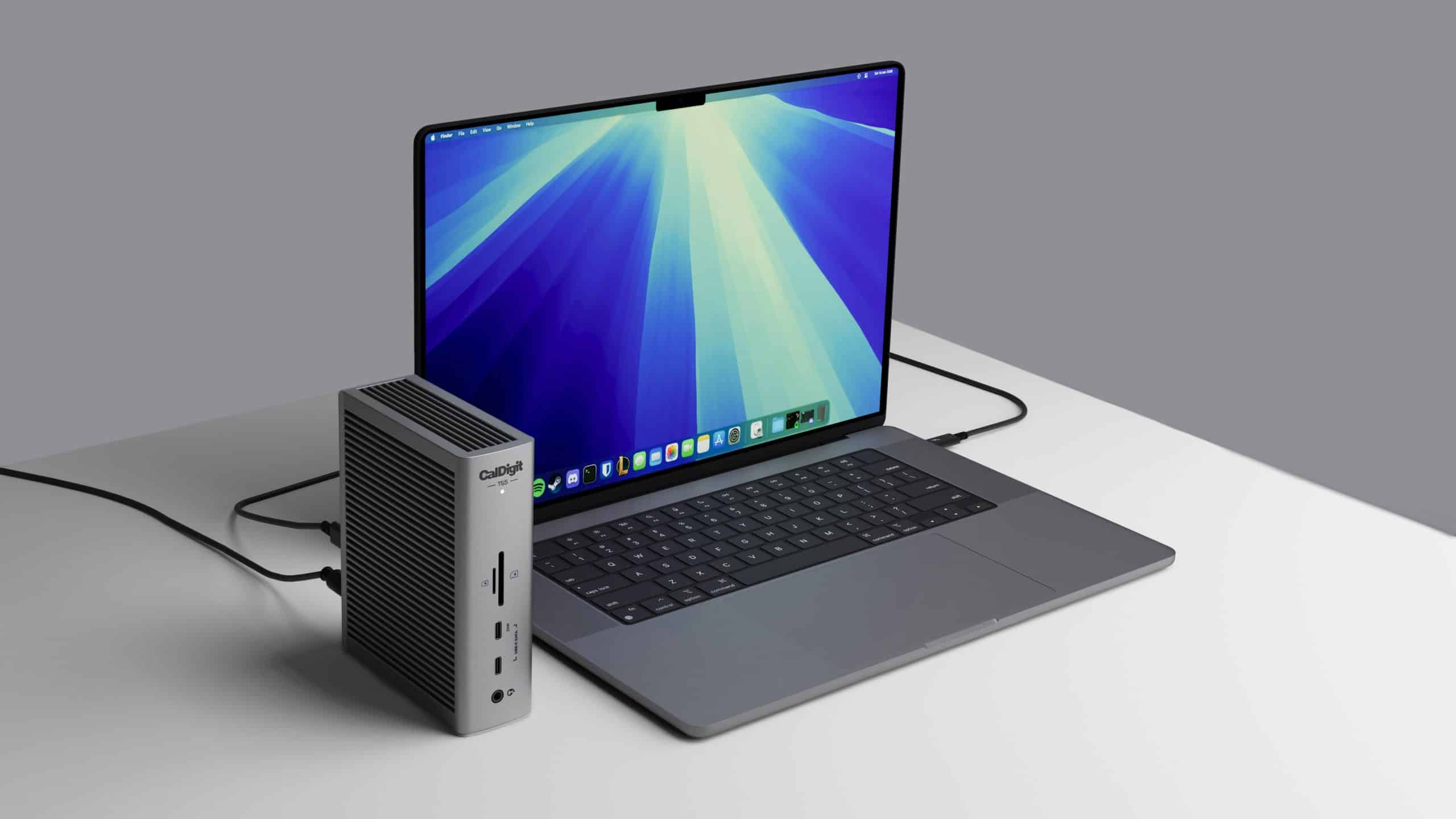 Szary laptop z niebiesko-zielonym tłem i czarną stacją dokującą obok.