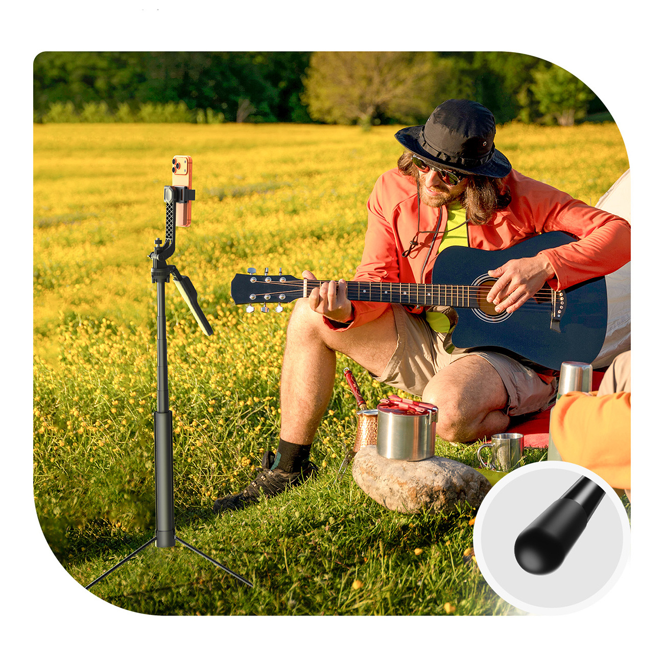 Mężczyzna gra na gitarze na zewnątrz obok statywu na telefon i pola żółtych kwiatów.