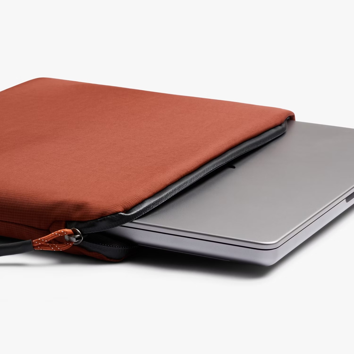 Srebrny laptop jest częściowo wkładany do rdzawej torby na laptopa z czarnym zamkiem.