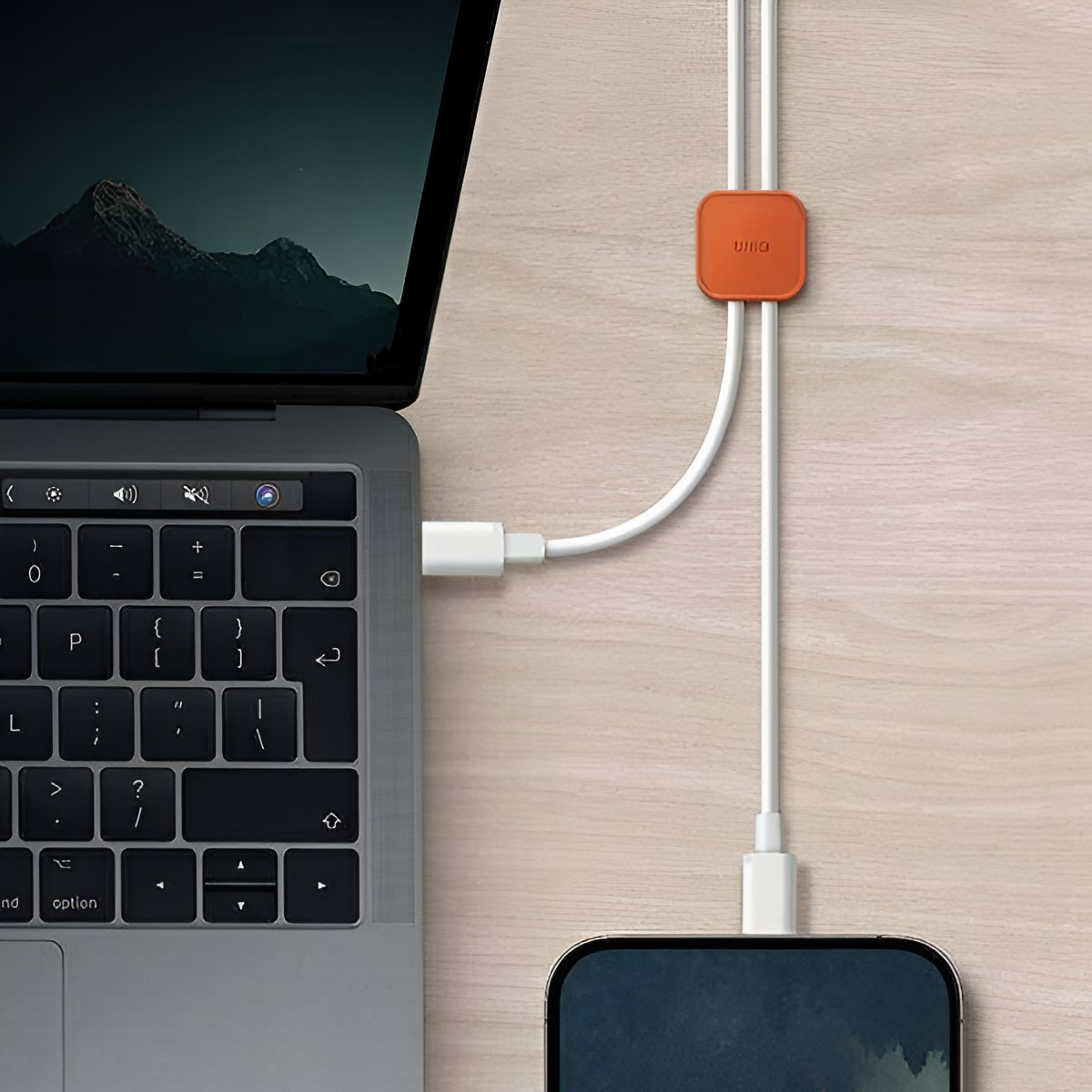 Laptop i telefon są połączone białymi kablami, zarządzanymi przez pomarańczowy klips.