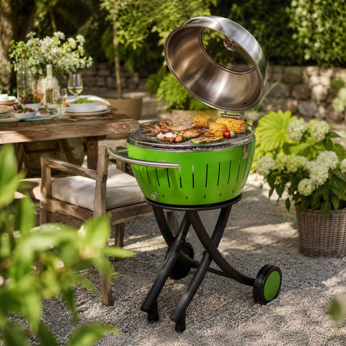 Zielony grill z otwartą pokrywą stoi na statywie na zewnątrz. Grillowane jest mięso i kolby kukurydzy.